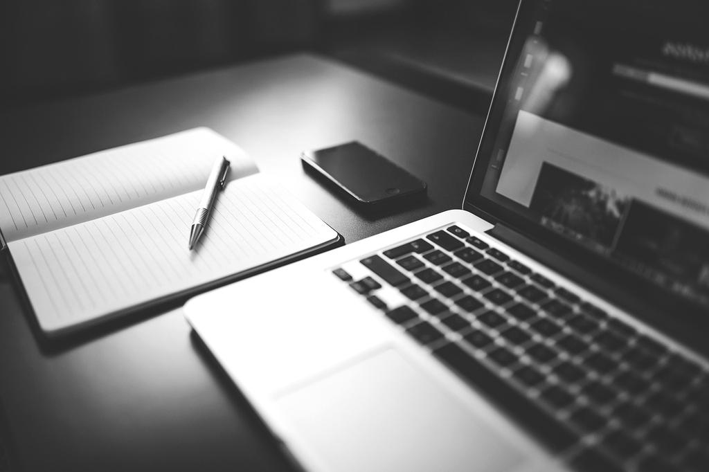Hands typing on laptop next to smartphone and notebook